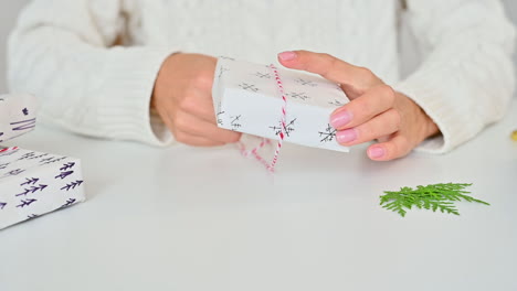 Female-Hands-Tie-The-Bow-Of-A-Gift-Box-With-Wrapping-Decorated-With-A-Pine-Branch-And-Snowflakes