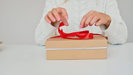 Woman-Unties-Red-Bow-Of-A-Box-And-Pulls-Out-A-Gift-In-A-Fabric-Bag