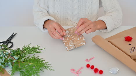 Female-Hands-Tie-The-Rope-Of-A-Gift-Box-With-Wrapping-Decorated-With-A-Pine-Branch-And-Snowflakes