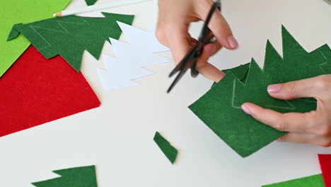 Manos-De-Mujer-Cortan-Un-árbol-De-Navidad-De-Tela-Verde-Con-Tijeras-Usando-Una-Plantilla