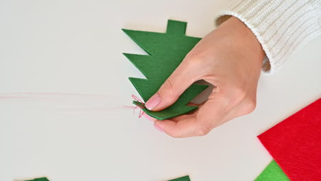 Woman-Hands-Sew-Two-Christmas-Trees-Cut-Out-Of-Green-Fabric-Using-Red-Thread