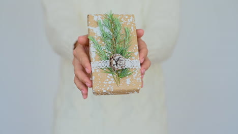 Woman-Shows-A-Wrapped-Gift-Decorated-With-A-Pine-Cone,-A-Branch-And-Painted-Snow