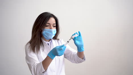 Female-Doctor-Wearing-Medical-Mask-Filling-A-Syringe-With-A-Vaccine-On-White-Background-And-Copy-Space