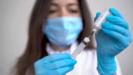 Female-Doctor-Wearing-Medical-Gloves-Filling-A-Syringe-With-A-Vaccine-For-Covid-19