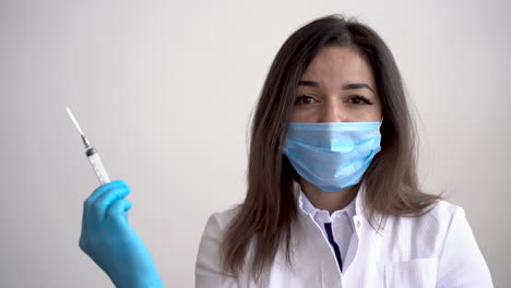 Portrait-Of-Female-Doctor-Wearing-Medical-Mask-And-Gloves-Holding-A-Syringe-With-A-Vaccine-For-Covid-19