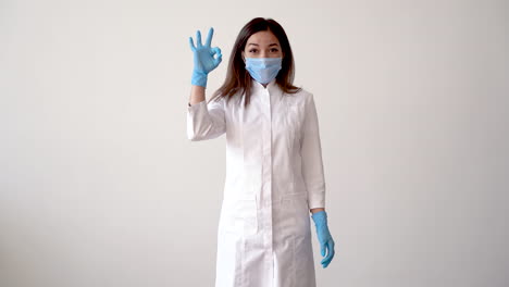 Female-Doctor-Putting-On-Medical-Mask-And-Making-The-Ok-Gesture