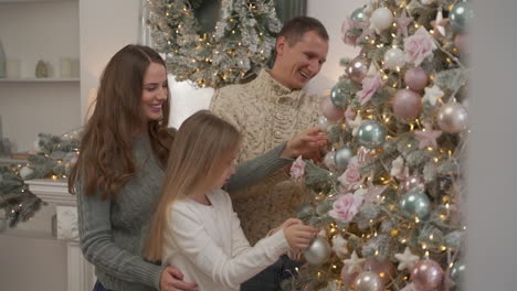 Mother,-Father-And-Little-Girl-Decorate-Christmas-Tree-With-Balls-And-Ornaments