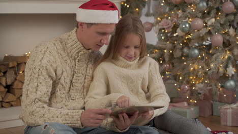 Vater-Und-Tochter-Verwenden-Zu-Weihnachten-Ein-Tablet-Mit-Einer-Weihnachtsmütze