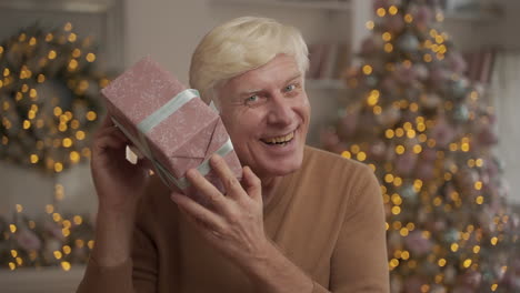 Portrait-Of-Old-Happy-Man-Holding-A-Christmas-Present-And-Looking-At-The-Camera