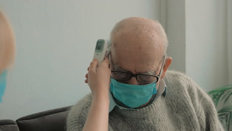 Die-Fürsorgliche-Krankenschwester-Misst-Die-Temperatur-Des-Alten-Mannes-Mit-Einem-Infrarot-Thermometer