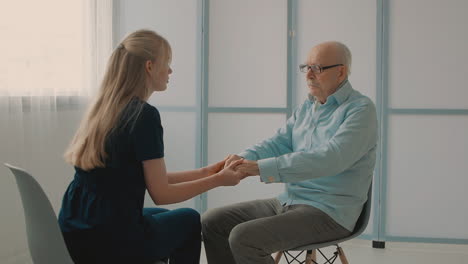 Young-Caring-Nurse-Talking-With-Very-Emotional-Elderly-Man-In-The-Office,-Holding-Hands