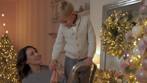 Junge-Schmückt-Weihnachtsbaum-Mit-Stern-Und-Ornamenten,-Seine-Mutter-Hilft-Ihm