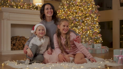 Mutter,-Kleiner-Junge-Und-Mädchen-Posieren-Und-Sagen-Hallo-Auf-Dem-Boden-Neben-Den-Geschenken-Und-Dem-Weihnachtsbaum-Sitzend