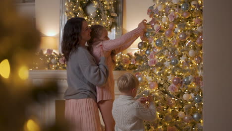 Niño-Y-Niña-Decoran-El-árbol-De-Navidad-Con-Bolas-Y-Adornos,-Madre-Levantándolos