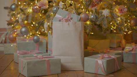 Hand-Take-A-Paper-Bag-With-Christmas-Gifts-Under-The-Tree
