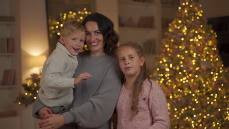 Mother,-Little-Girl-And-Boy-Looking-To-Camera-And-Waving-Hand-On-Christmas