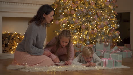 Little-Boy-And-Girl-Write-A-Letter-With-Their-Mother-On-The-Floor-Next-To-The-Gifts-And-The-Christmas-Tree
