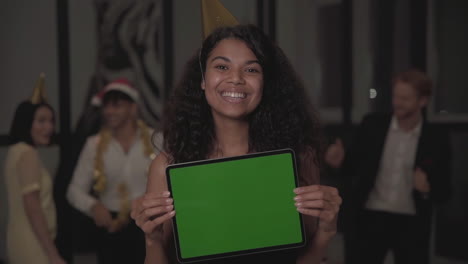 Young-Happy-Black-Woman-Holding-A-Tablet-With-Mockup-Green-Screen-And-Looking-At-The-Camera-At-New-Year's-Eve-Party