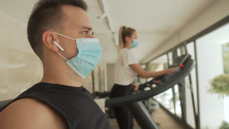 Young-athlete-male-and-female-with-face-mask-using-exercise-machines-in-the-gym