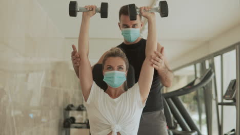 Athlete-Woman-Lifts-Weights-And-Man-With-Face-Mask-Exercising-In-The-Gym