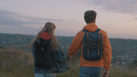 --Young-male-and-female-hikers-with-backpacks-reaching-the-top-of-the-mountain