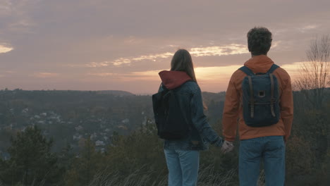 -Young-couple-of-hikers-with-backpacks-reaching-the-top-of-the-mountain