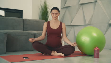 Young-Pretty-Pregnant-Woman-Doing-Yoga-In-Lotus-Pose-And-Meditating,-Wearing-Sportswear-At-Home