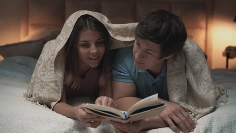 Young-Couple-Reading,-Covered-With-A-Blanket