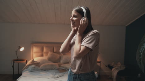 Young-Woman-With-Headphones-Listening-To-Music-And-Dancing-In-Bedroom-At-Night
