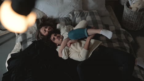 Young-Romantic-Playful-Couple-Lying-In-Bed-Hugging-And-Wearing-Winter-Clothes