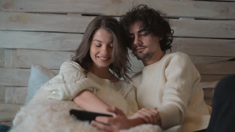 Young-Cute-Couple-In-Bed-Watching-Something-Funny-On-The-Phone