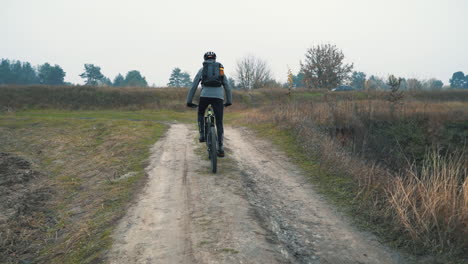 Cyclist-With-Backpack-Riding-A-Mountain-Bike-Down-The-Road-In-The-Countryside