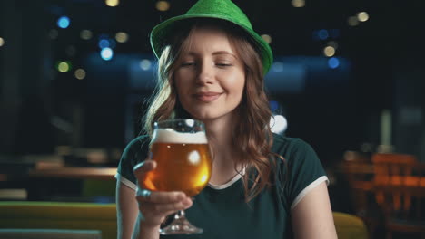 Porträt-Einer-Hübschen-Jungen-Frau,-Die-Mit-Einem-Bier-Anstößt-Und-Einen-Irischen-Grünen-Hut-Trägt