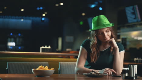 Hübsche-Junge-Frau,-Die-Eine-App-Mit-Dem-Smartphone-Verwendet-Und-Einen-Irischen-Grünen-Hut-Trägt