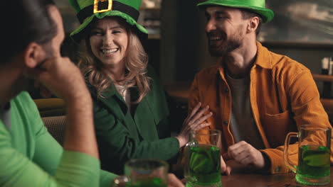 Hombres-Jóvenes-Y-Mujeres-Hermosas-Con-Sombreros-Irlandeses-Divirtiéndose-Con-Jarras-De-Cerveza-Verde