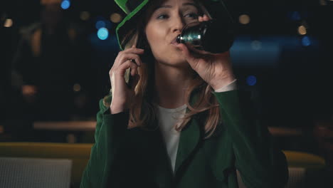 Porträt-Einer-Blonden-Frau,-Die-Ein-Smartphone-Benutzt,-Ein-Bier-Trinkt-Und-Einen-Irischen-Grünen-Hut-Trägt