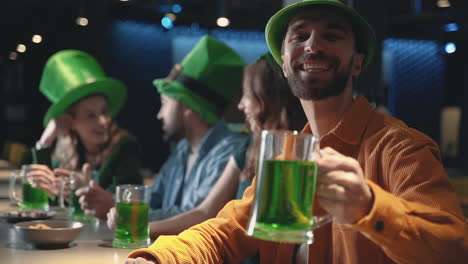 Freunde-Feiern-Den-St-Patrick&#39;s-Day-In-Einer-Kneipe,-Lächelnder-Glücklicher-Mann-Schaut-In-Die-Kamera-Und-Stößt-Mit-Einem-Krug-Bier-An