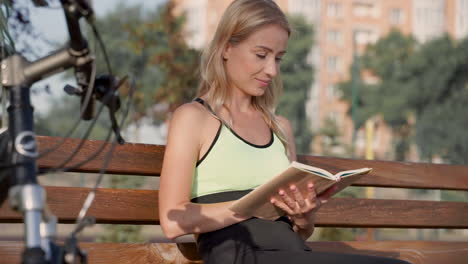 Happy-Athlete-Woman-Reading-A-Book-Sitting-On-A-Bench-Outdoors