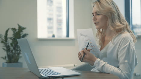 Pretty-Young-Blonde-Woman-Having-A-Business-Video-Call-And-Showing-Documents-With-Charts-And-Graphs