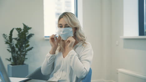 Pretty-Young-Blonde-Business-Women-Put-On-Face-Mask-To-Work-Together-Indoors-In-The-Office