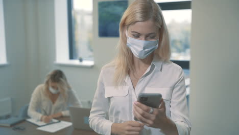 Business-Woman-With-Face-Mask-Having-A-Business-Video-Call-Holding-A-Smartphone-In-The-Office