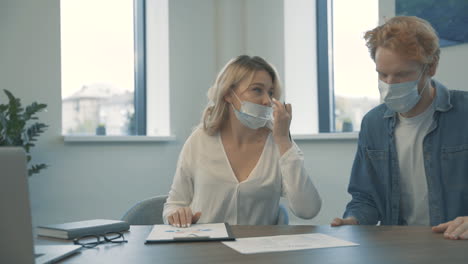 Young-Business-Woman-And-Man-With-Face-Mask-Do-Elbow-Bump-And-Discuss-Work-In-The-Office