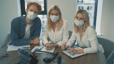 Young-Business-Women-And-Man-With-Face-Mask-Looking-At-Camera-In-The-Office