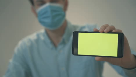 Businessman-With-Face-Mask-Holding-A-Green-Screen-Smartphone
