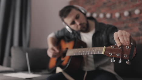 Young-Male-Musician-Playing-And-Adjusting-Guitar-At-Home