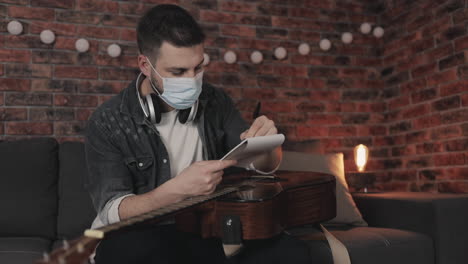 Young-Musician-Man-With-Medical-Face-Mask-Creating-Music,-Having-Ideas,-Taking-Notes-At-Home-During-Lockdown-Due-To-The-Covid-19-Pandemic