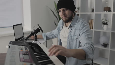Male-Musician-Playing-Electric-Keyboard-And-Using-A-Laptop-At-Home-1