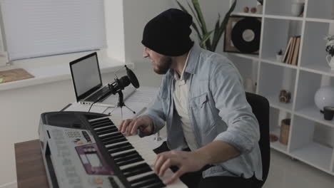 Male-Musician-Singing,-Playing-Electric-Keyboard-And-Using-A-Laptop-At-Home-1