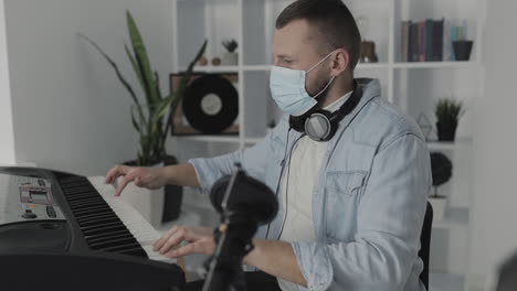 Male-Musician-With-Medical-Face-Mask-Playing-Electric-Keyboard-At-Home-During-Lockdown-Due-To-The-Covid-19-Pandemic