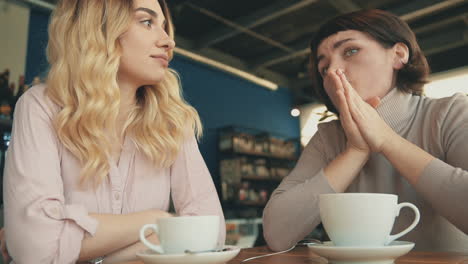 Blonde-And-Brunette-Female-Friends-Sharing-Moments-And-Talking-In-A-Coffee-Shop